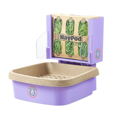 Assembled on a white background, the purple BunnyLet includes the assembly of both the HayPod and litter box. The HayPod is open, revealing a picture filled with fresh green hay inside. The image captures the vibrant scene of the assembled BunnyLet with an abundance of fresh hay in the open HayPod.