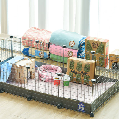 Stylish setup of GuineaDad Piggy Condo C&C Cage in a home environment, accompanied by GuineaDad accessories like Liners and Play Package, illustrating a comfortable and practical guinea pig habitat.